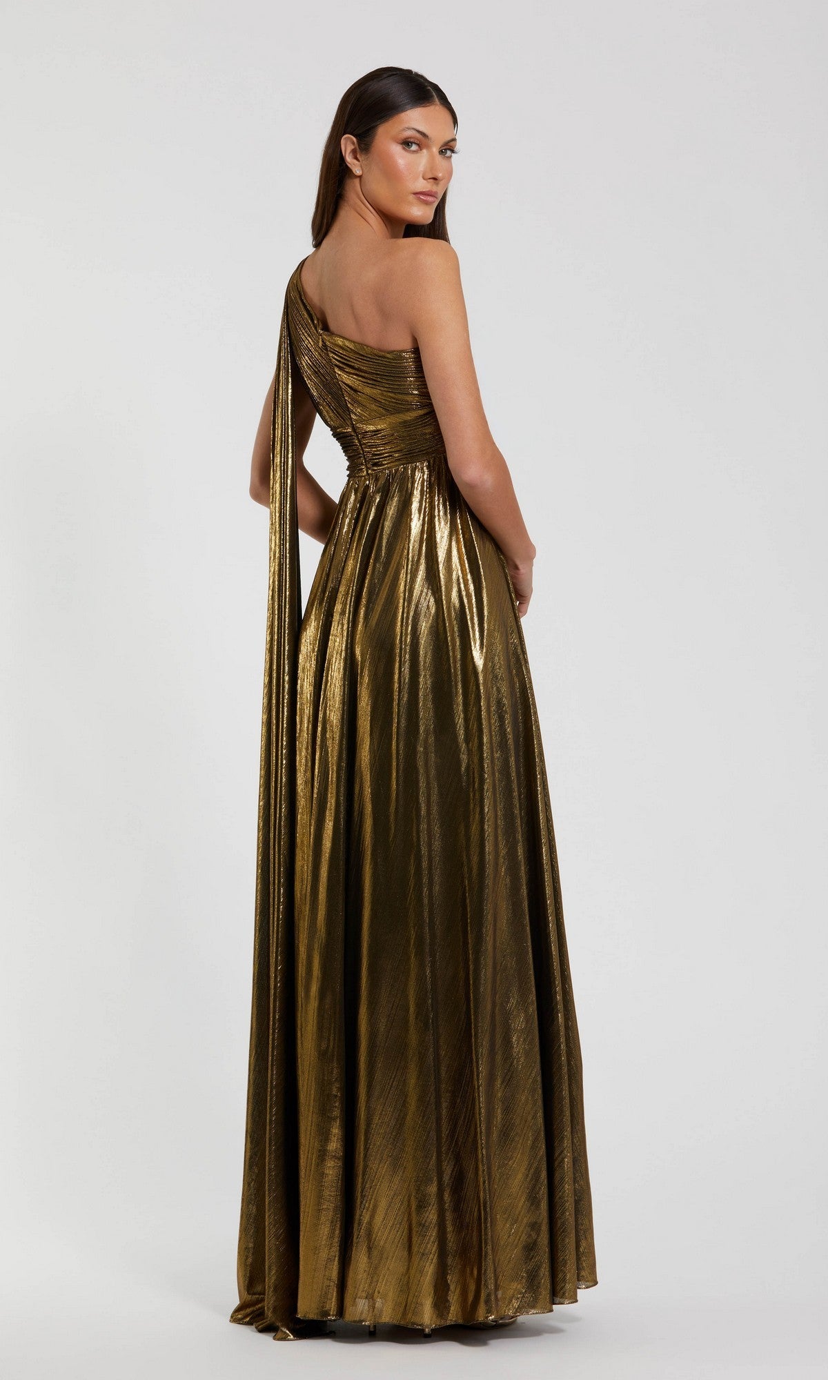 A woman stands with her back to the camera against a plain white background, modeling the Mac Duggal 56086 long formal dress—a shimmering metallic one-shoulder gown.