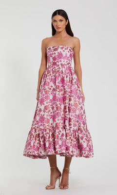A woman stands against a plain background in the Midi Wedding Guest Dress: Mac Duggal 56092 in Pink Multi, featuring a strapless silhouette with floral brocade and a ruffled hem—an elegant choice for any wedding guest.