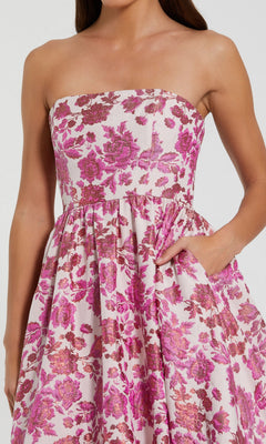 A woman in the Midi Floral Wedding Guest Dress: Mac Duggal 56092—a strapless pink and magenta midi with a fitted bodice, gathered skirt, and pockets—makes an ideal choice for wedding guests.