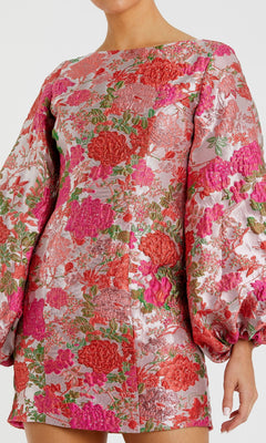 Someone is wearing the Mac Duggal 56106 Short Floral Wedding Guest Dress, a long-sleeved pink and red brocade cocktail dress featuring a high neckline and voluminous sleeves.