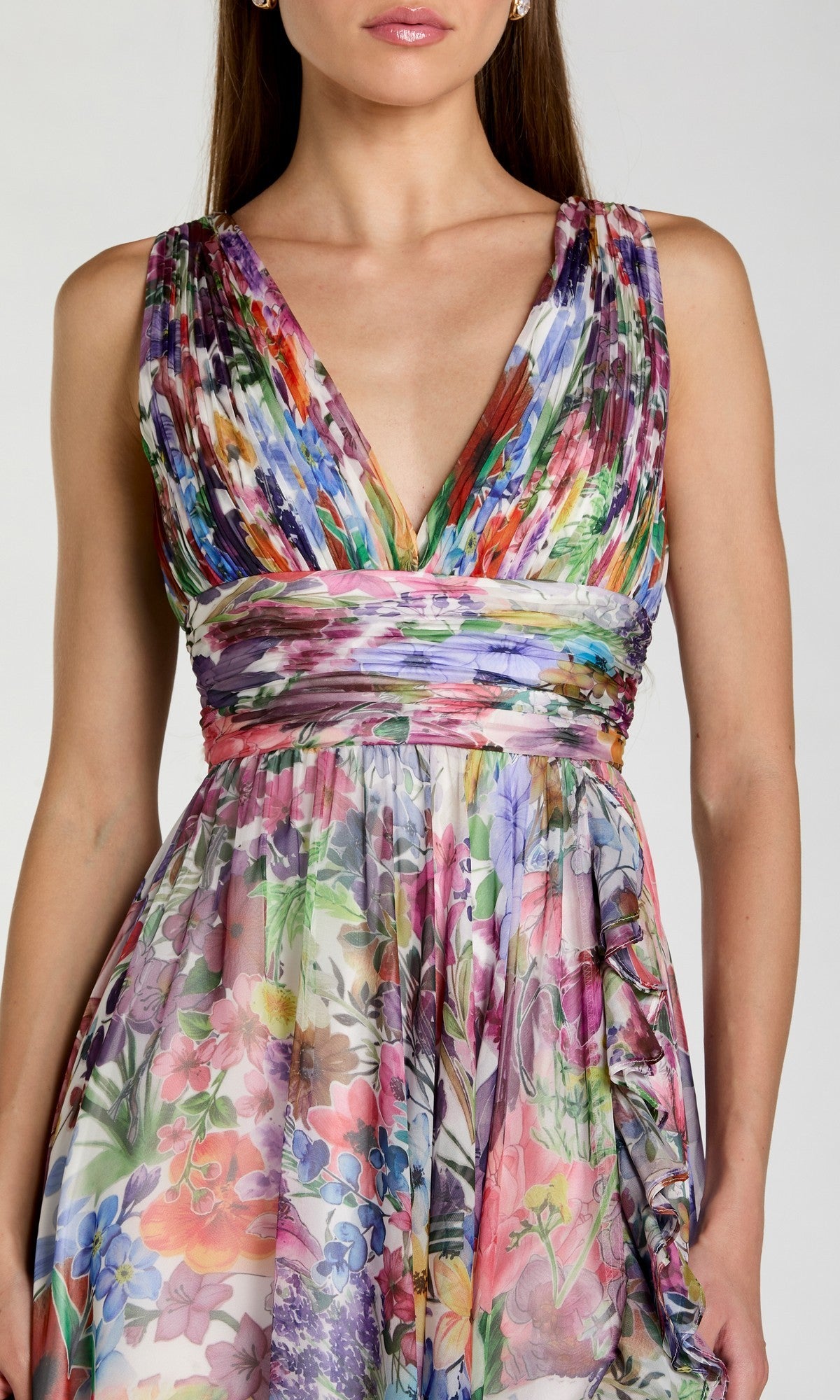 A woman wearing the Mac Duggal 56119 long prom dress—a sleeveless, V-neck gown crafted from floral chiffon with a multicolored pattern, featuring a ruched waist detail and a flowing A-line skirt.