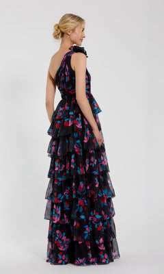 A woman in the Mac Duggal 56120 Long Print Ruffled Formal Dress—black, sleeveless, tiered, with colorful floral patterns—stands sideways against a plain light background.