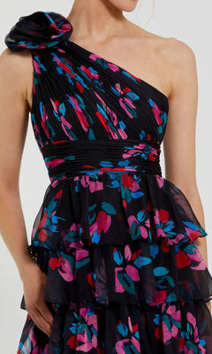A woman wears the Mac Duggal 56120 Long Print Ruffled Formal Dress, featuring a one-shoulder design with layered ruffles and a vibrant red, blue, and purple floral pattern.