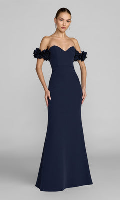 A woman stands against a plain gray background wearing the Mac Duggal 56131 Floral-Straps Long Formal Dress, a navy blue, off-the-shoulder evening gown with elegant crepe fabric and floral strap detailing.