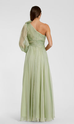 A woman stands with her back turned, wearing the Mac Duggal 56142 long formal dress—a sage-green, one-shoulder chiffon evening gown featuring a single sheer sleeve and a flowing skirt.