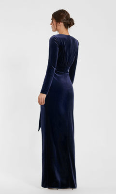 A woman faces away, wearing the Mac Duggal 56143 long formal dress, featuring velvet fabric, long sleeves, a fitted waist, and a back slit.