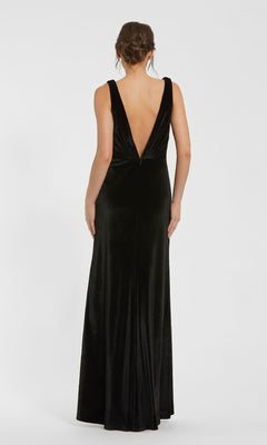 A woman faces away, wearing the Mac Duggal 56144 long black velvet formal dress with a deep V-back, set against a plain white background.