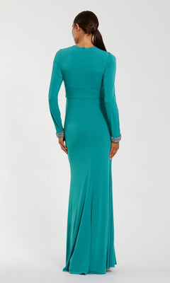 A woman stands with her back to the camera against a plain background, wearing the Mac Duggal 56150 long formal dress—a floor-length teal jersey gown with long sleeves and jeweled cuffs.