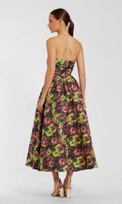 A woman stands in profile with her hair in a ponytail and gold high-heeled sandals, wearing the Mac Duggal 56165 Tea-Length Party Dress featuring a strapless floral design, fitted bodice, and full skirt.