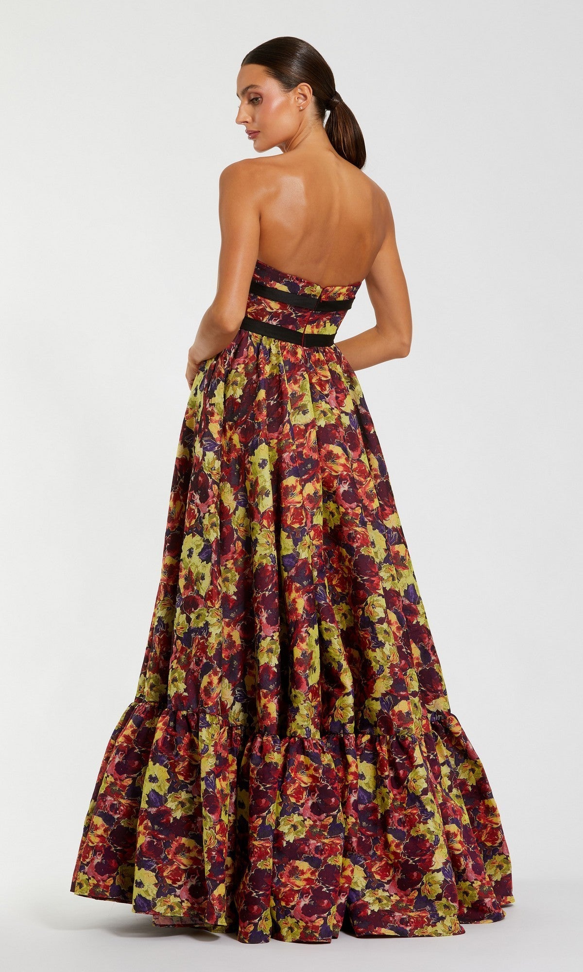 A woman wearing the Mac Duggal 56166 long formal dress, featuring a strapless brocade design with a fitted bodice and full skirt, stands against a plain background, facing away while turning her head slightly to the side.