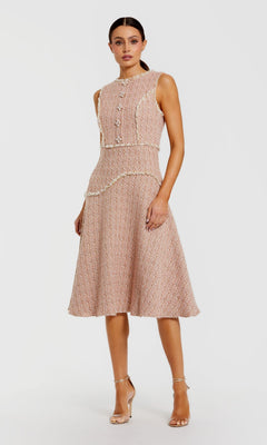 A woman stands against a plain white background, wearing the Mac Duggal 56172 Button-Up Boucle Midi Dress—a sleeveless, knee-length textured pink dress featuring a fitted waist, decorative faux pearl buttons, cream trim—and nude high-heeled sandals.