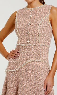 Wearing the Button-Up Boucle Midi Dress (Mac Duggal 56172), a woman stands with one hand on her hip; the textured, sleeveless pink dress features decorative faux pearl buttons and white fringe trim.