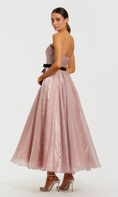 A woman wearing the Mac Duggal 56184 long formal dress in pink organza, featuring a strapless neckline, ankle-length hem, and black waistband, paired with silver high heels, poses against a plain white background.