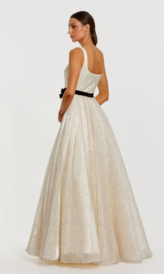 A woman wearing the Mac Duggal 56185 long formal dress—an organza, sleeveless, floor-length A-line gown adorned with small sparkly dots and a black waist belt—stands looking over her shoulder.