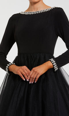 A woman in the Mac Duggal 56186 long sleeve black formal gown with pearl-embellished collar and cuffs stands with her hands clasped.