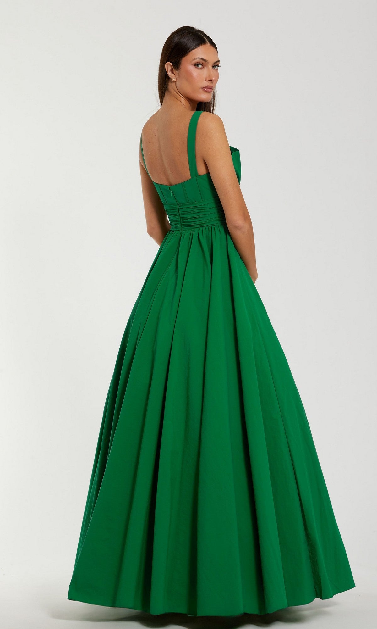 A woman wearing the Mac Duggal 56189 long formal dress—a sleeveless, floor-length ballgown in luxurious green faille—stands turned slightly away from the camera against a plain background.