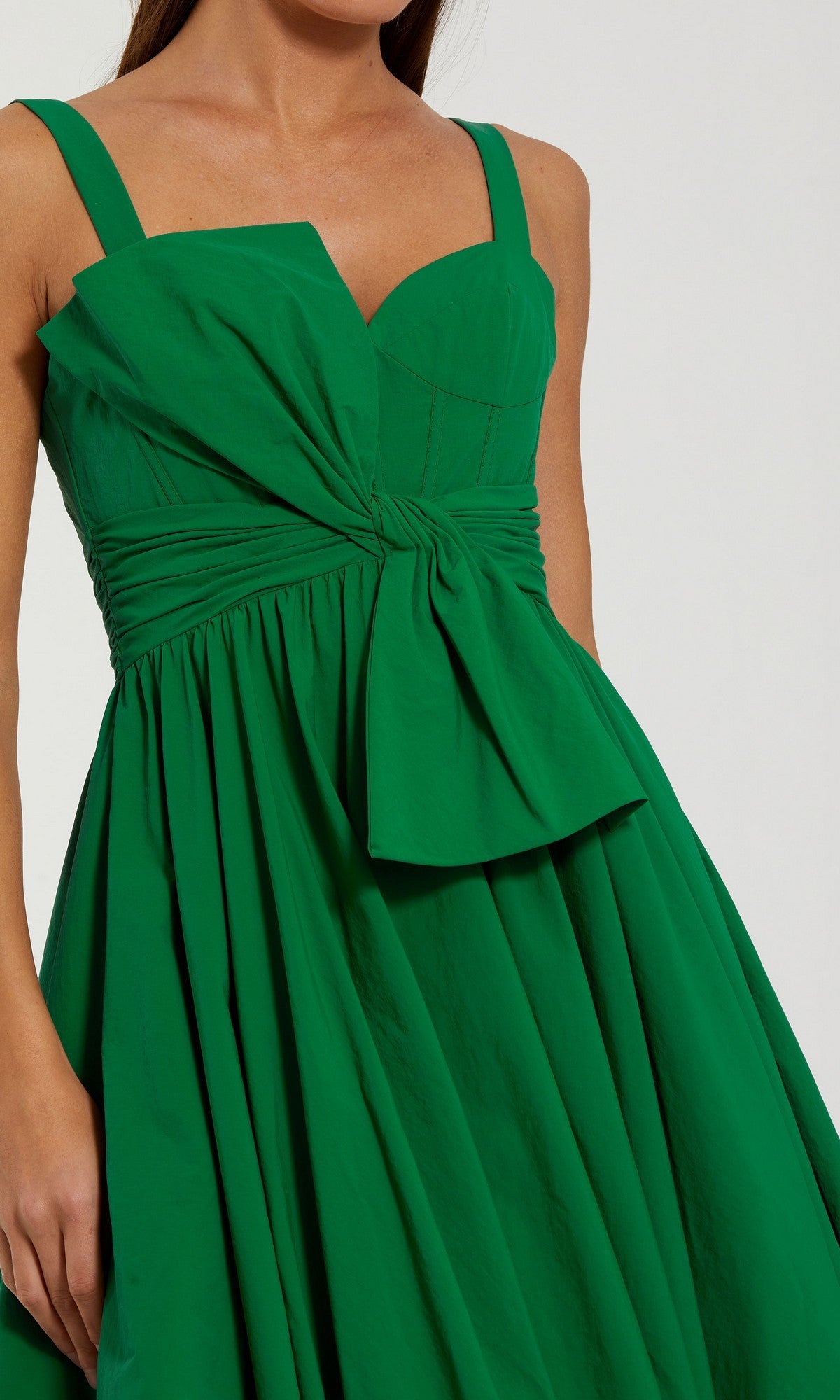 A woman wears the Long Formal Dress: Mac Duggal 56189—a sleeveless, fitted green gown crafted from luxurious faille fabric, featuring a statement bow at the waist and a flared skirt for an elegant, ballgown-inspired look.