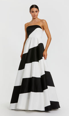 A woman stands gracefully against a plain white background, wearing the Mac Duggal 56190 Black and White Long Formal Gown featuring bold horizontal stripes and a strapless design.