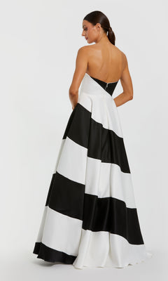 A woman stands facing away in the Mac Duggal 56190 black and white long formal gown, featuring wide horizontal stripes, a strapless neckline, and an elegant A-line silhouette.