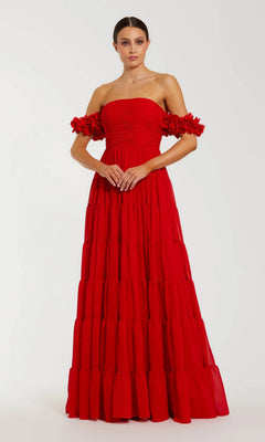 A woman wearing the Mac Duggal 56191 long formal dress in red, featuring an off-the-shoulder neckline, a floor-length ruffled tiered skirt, and striking 3D floral sleeves, stands against a plain light background.