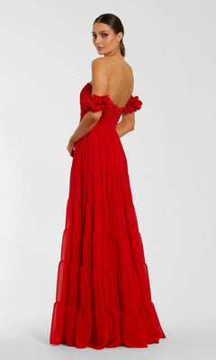 A woman wears the Mac Duggal 56191 Long Formal Dress—a floor-length, red chiffon off-the-shoulder gown featuring ruffle accents and delicate 3D floral sleeves—as she stands against a plain light background, glancing over her shoulder.