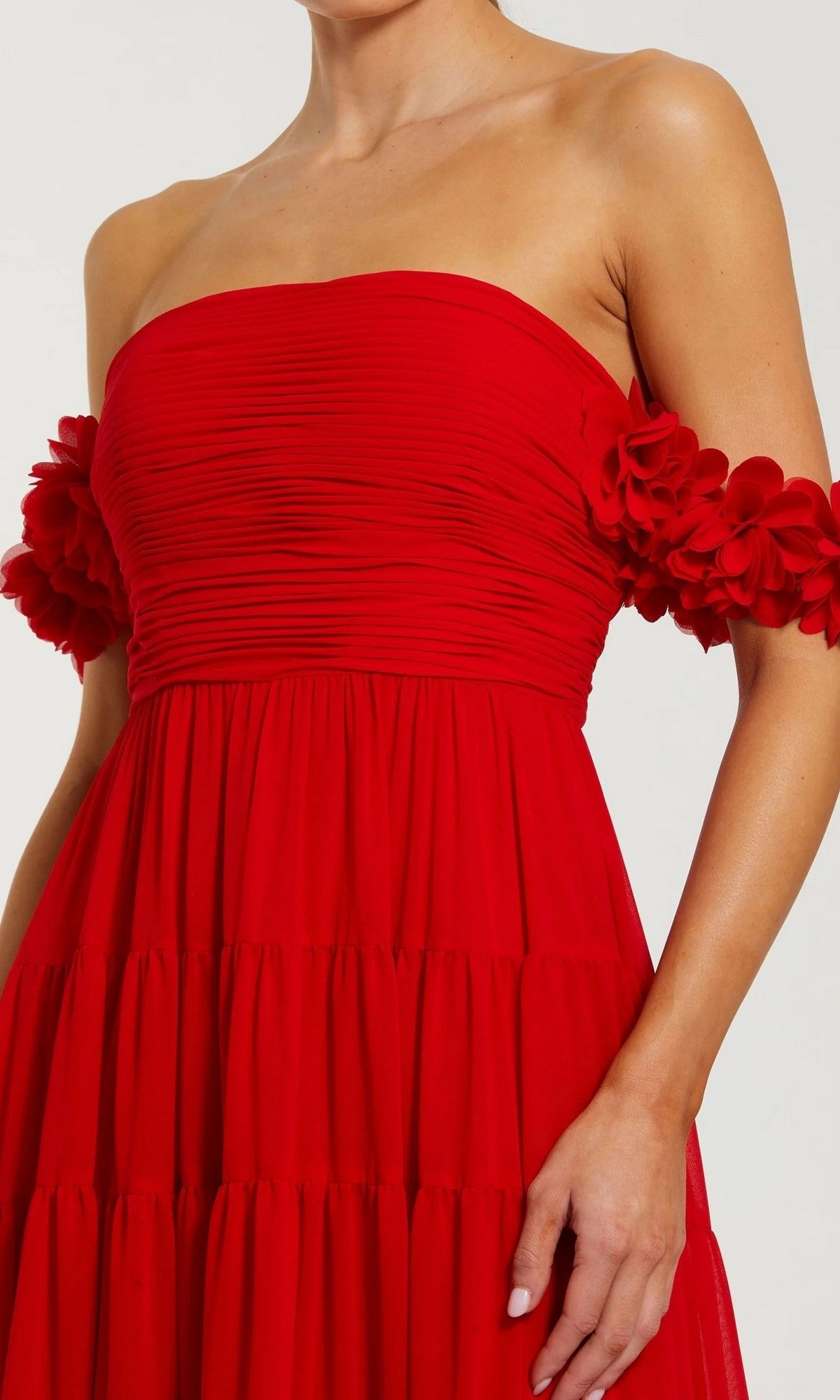 A woman is wearing the Mac Duggal 56191 long formal dress—a strapless, ruched red chiffon gown with off-the-shoulder 3D floral sleeves; her head is not visible in the image.