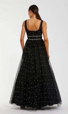 A woman with long brown hair in a low ponytail wears the Mac Duggal 56204 long formal dress—an A-line black ball gown with a floor-length tulle skirt and white polka dots—seen from the back against a plain white background.