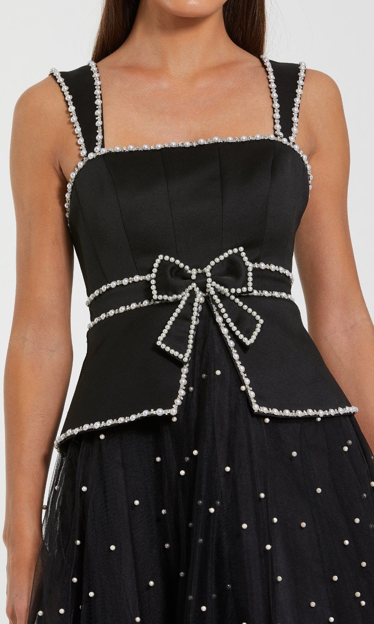 A woman wearing the Mac Duggal 56206 Black Midi Wedding Guest Dress, featuring a sleeveless top with pearl trim and bow at the waist, paired with a black tulle skirt with pearl-like embellishments—a chic vintage-inspired look.