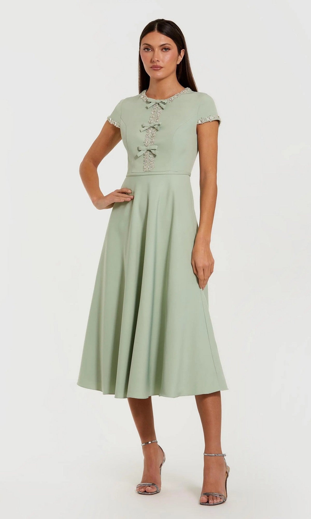 A woman stands in heels against a plain background, wearing the Midi Party Dress: Mac Duggal 56242—a light green, short-sleeve midi dress with decorative buttons.