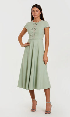 A woman stands in heels against a plain background, wearing the Midi Party Dress: Mac Duggal 56242—a light green, short-sleeve midi dress with decorative buttons.
