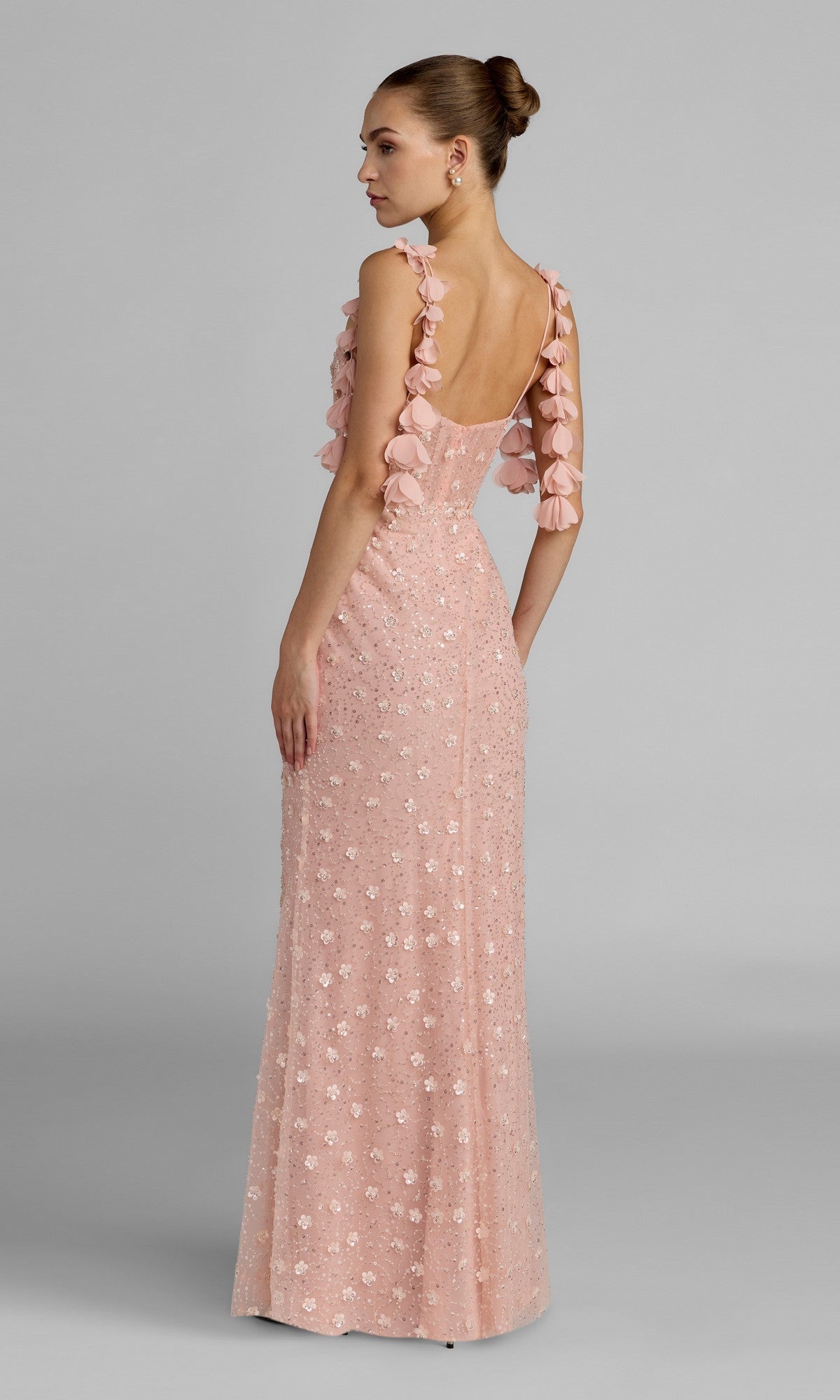 A woman in profile stands against a plain gray background wearing the Mac Duggal 56259 long formal dress, a pale pink sleeveless gown adorned with intricate 3D floral embellishments.