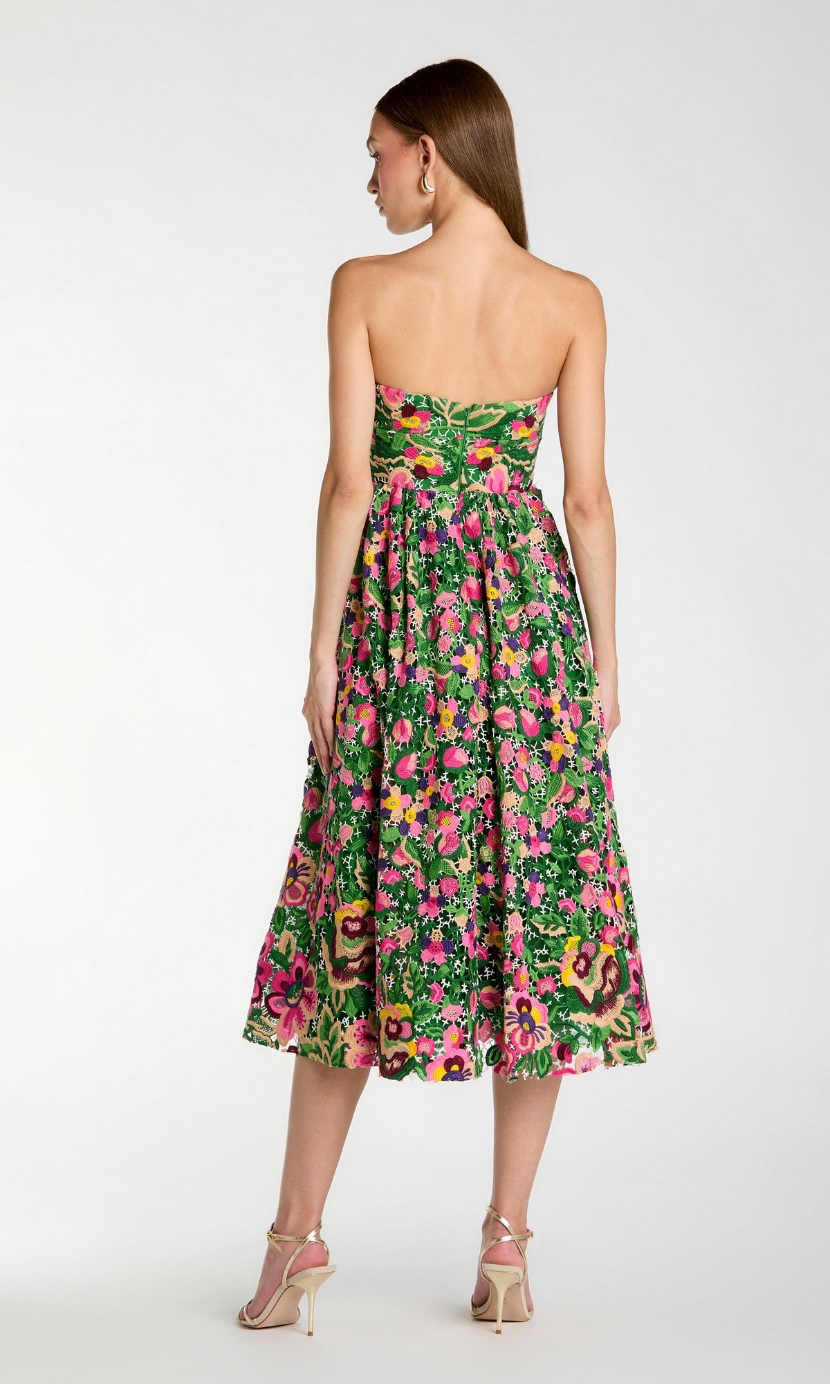Woman facing away, wearing the Mac Duggal 56265 midi party dress in green and pink with delicate floral embroidery, showcasing a strapless fitted bodice and flared skirt, paired with beige heels against a plain background.
