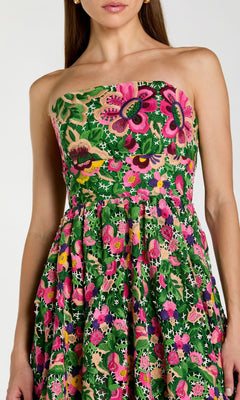 A woman stands against a plain background wearing the Midi Party Dress: Mac Duggal 56265—a striking strapless midi party dress adorned with a vibrant floral pattern in shades of green, pink, purple, and yellow.