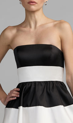 A woman models the Mac Duggal 56281 Tea-Length Party Dress, a strapless black and white color-blocked design, pictured from shoulders to hips against a plain gray background.
