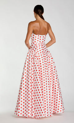 A woman stands facing away against a plain background, wearing the Mac Duggal 56283 long formal dress—a strapless ballgown adorned with red polka dots.