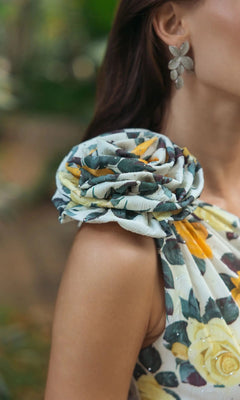 A woman, shown from the neck down, wears the Mac Duggal 56314 Midi Party Dress—a sleeveless floral-printed charmeuse style featuring a statement fabric flower on the shoulder—paired with leaf-shaped earrings.