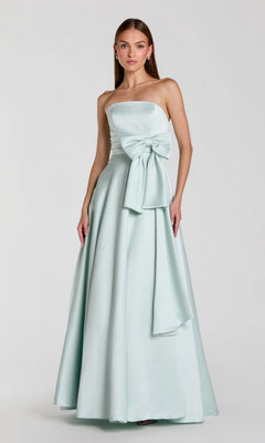 A woman wearing the Long Formal Dress: Mac Duggal 56318 in seafoam, a strapless satin gown with a floor-length silhouette and a large bow at the waist, stands against a plain light background.