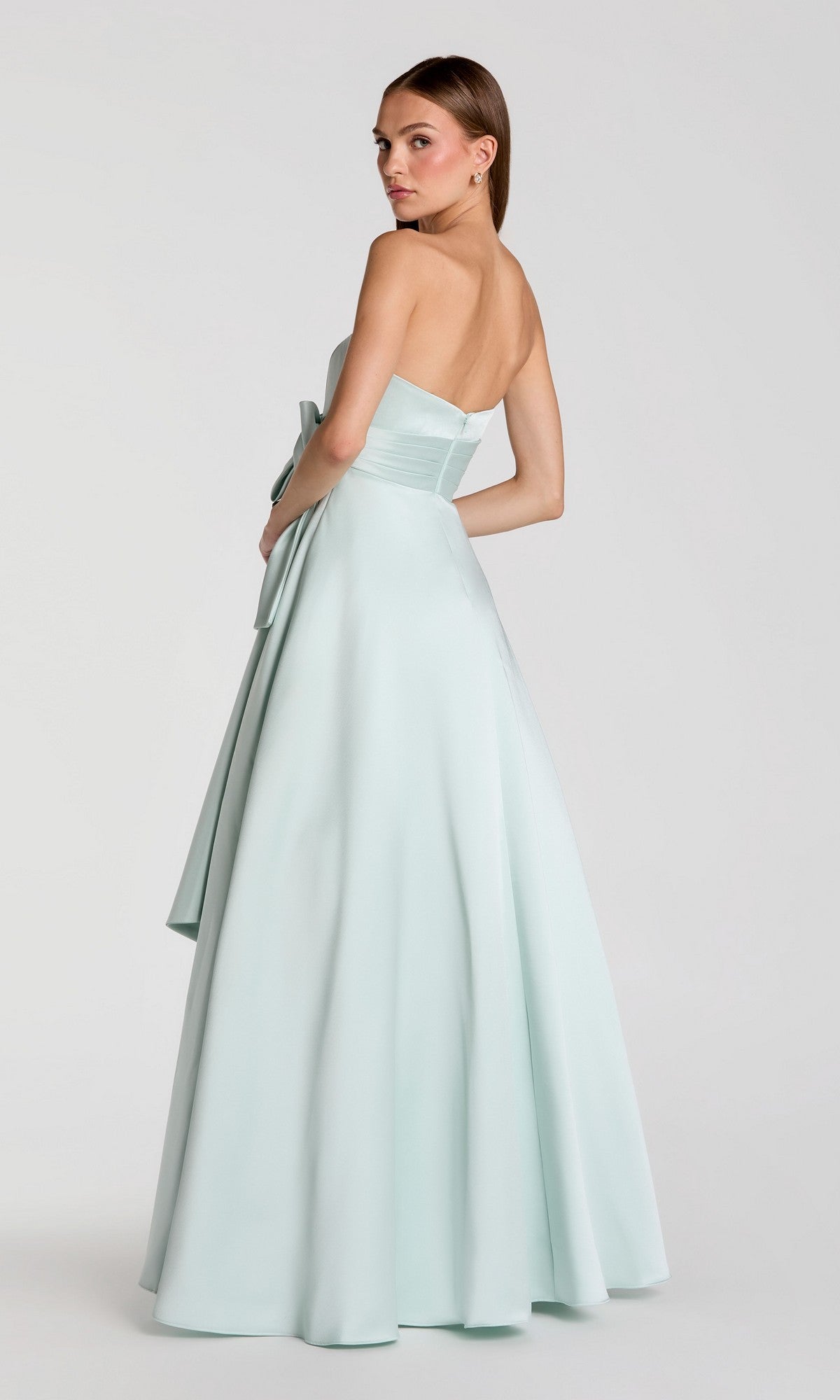 A woman wearing the Mac Duggal 56318 long formal dress—strapless, satin, light blue, and floor-length—stands facing away and glances over her shoulder against a plain light background.
