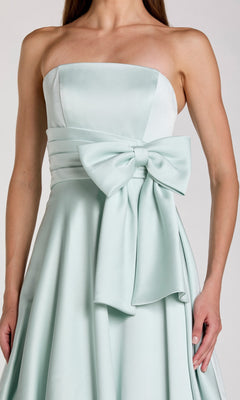 A woman wearing the Mac Duggal 56318 long formal dress—a strapless satin gown in light blue featuring a wide waistband and a large bow on the front, exuding elegant style.