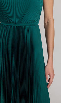 A person is wearing the Mac Duggal 56326 midi party dress, featuring a sleeveless, pleated dark green design with a modest A-line skirt, standing against a plain light background with one arm visible.