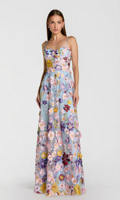 A woman in a sleeveless, floor-length Mac Duggal 56331 long formal dress in powder blue multi, adorned with colorful floral embroidery, stands against a plain white background. This elegant piece is perfect for any sophisticated occasion.