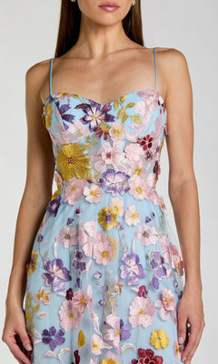 A woman models the Mac Duggal 56331 Long Formal Dress, featuring a blue hue with thin straps and multicolored floral embroidery; she is shown from shoulders to knees against a plain background.