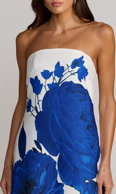A woman wearing the Mac Duggal 56344 long formal dress, a strapless white gown featuring bold blue floral prints, is photographed from shoulders to thighs against a neutral background.