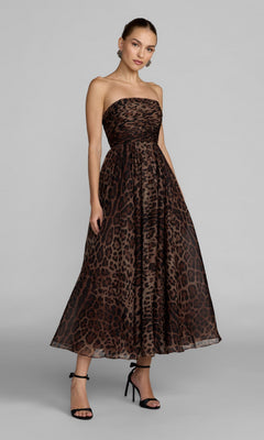 A woman stands against a light gray background wearing the Strapless Leopard Formal Dress: Mac Duggal 56350—an ankle-length, leopard print design with an a-line skirt—paired with black high-heeled sandals.