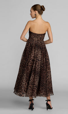 A woman wearing the Mac Duggal 56350 Strapless Leopard Formal Dress—an ankle-length, strapless gown with an a-line skirt—stands facing away in black high heels, her hair styled in a bun, against a plain light-colored background.