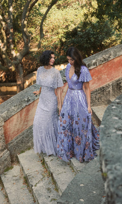 Two women in Long Formal Dress 5637 by Mac Duggal, featuring elegant floor-length A-line silhouettes and v-necklines, walk down outdoor stone steps amidst greenery and sunlight.