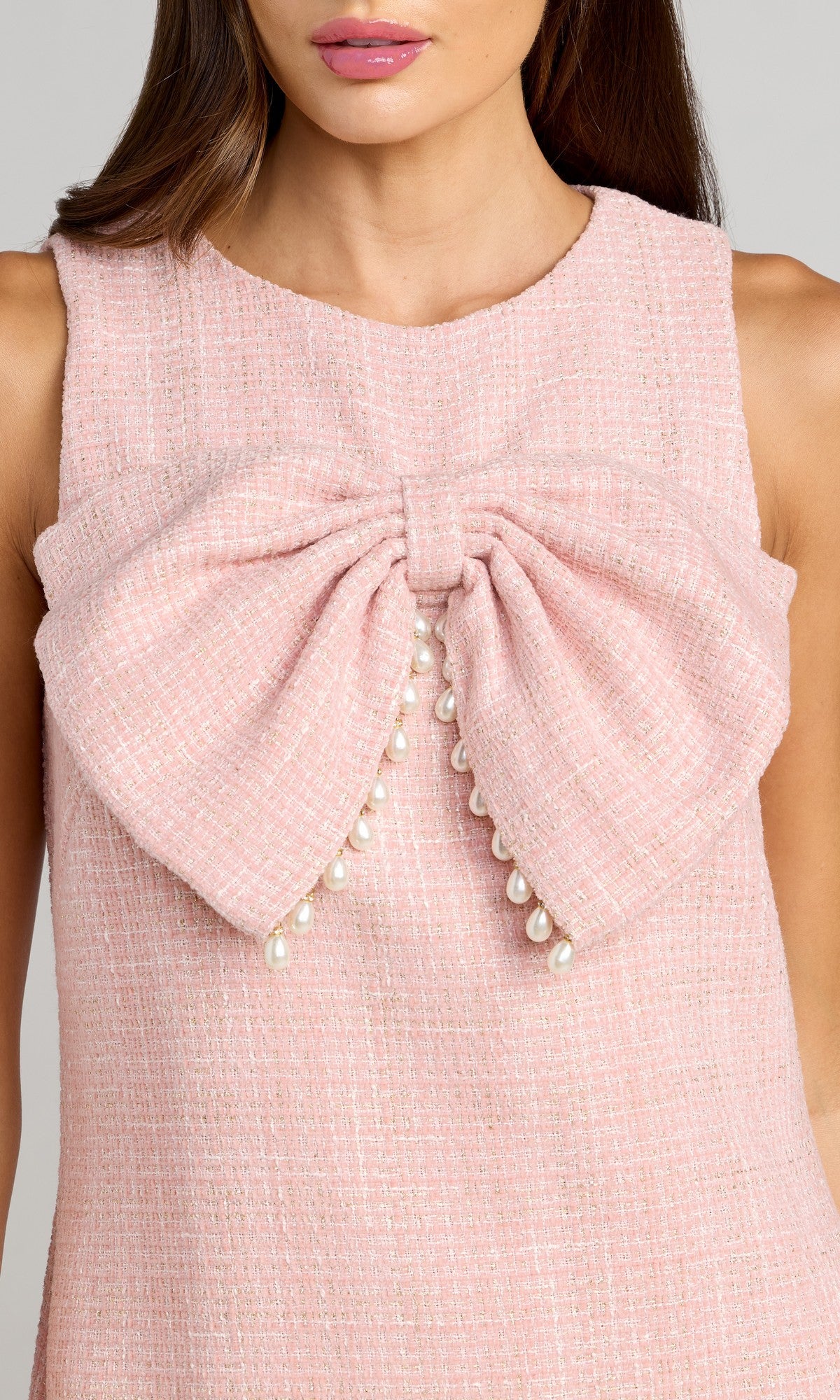 A woman wearing the Mac Duggal 56370 Short Boucle Shift Dress, a sleeveless pink textured dress featuring a large bow with pearl accents at the front.