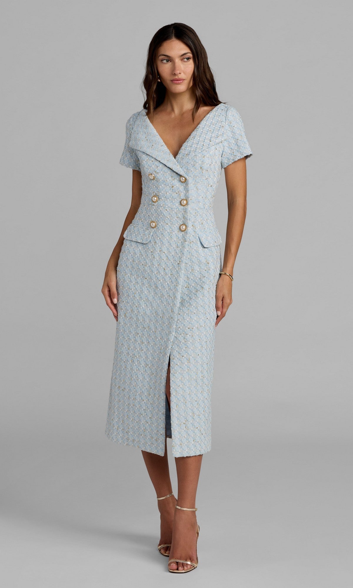 A woman wearing the Mac Duggal 56374 Tea-Length Party Dress in powder blue, featuring short sleeves, double-breasted gold buttons, and front pockets, stands in neutral high-heeled sandals against a plain gray background.