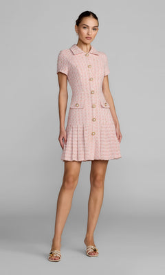 A woman stands in a studio wearing the Mac Duggal 56379 Short Party Dress in pink, featuring short sleeves, a pleated A-line silhouette, front pockets, and a textured button-down design, paired with open-toe heels.