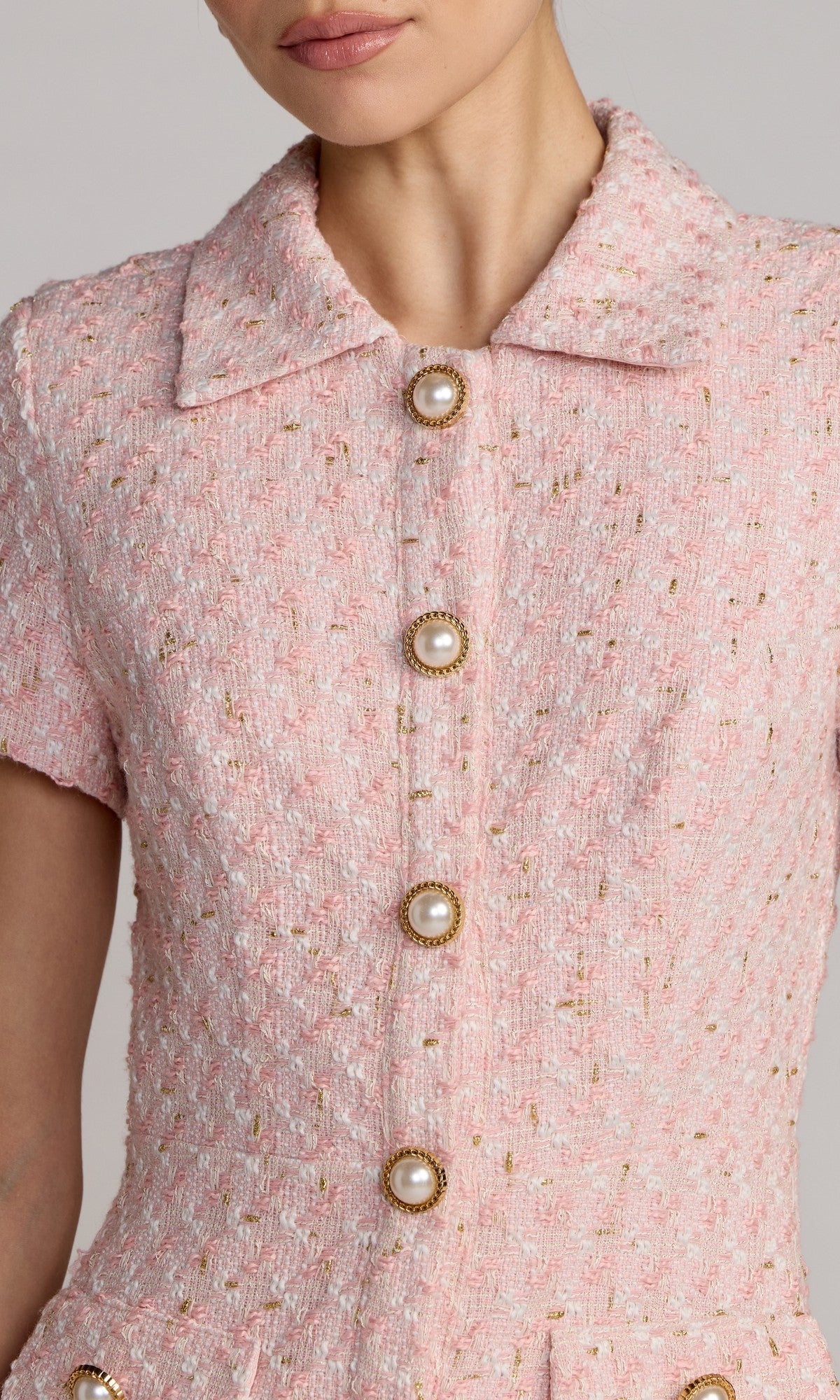 A close-up of a person wearing the Mac Duggal 56379 short party dress, featuring short sleeves, pink textured boucle fabric, a collar, and four pearl buttons down the front.